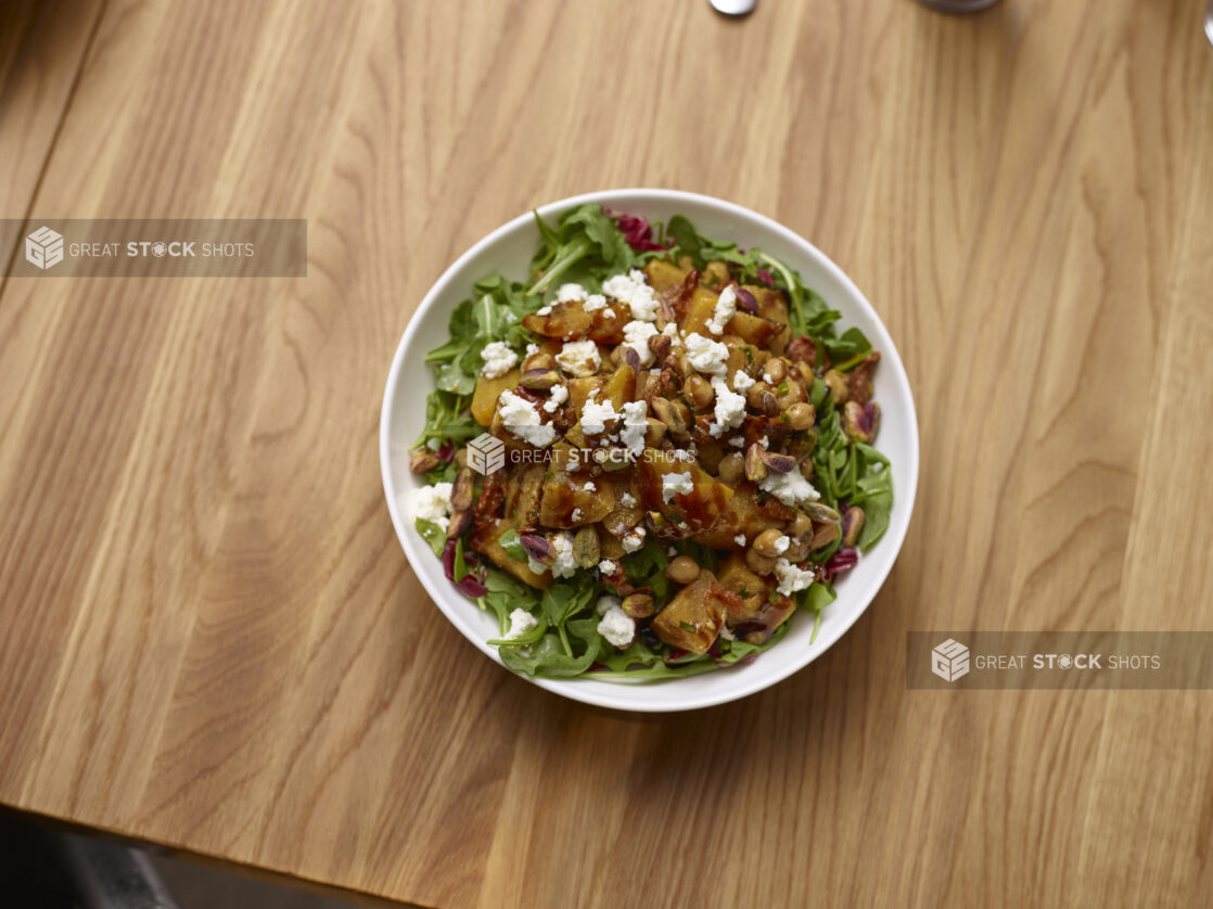 Chopped Leafy Vegetable Salad with Golden Beets, Feta Cheese and Roasted Chick Peas in a Round White Ceramic Salad Bowl on a Wooden Table