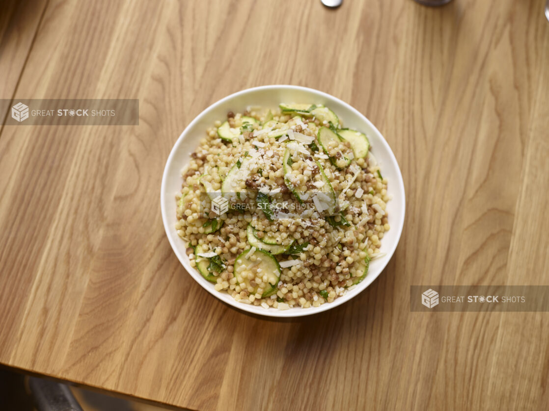 Fregola Sarda Pasta Salad with Zucchini in a Round White Ceramic Salad Bowl on a Wooden Table