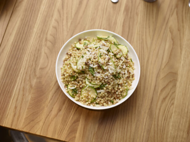 Fregola Sarda Pasta Salad with Zucchini in a Round White Ceramic Salad Bowl on a Wooden Table