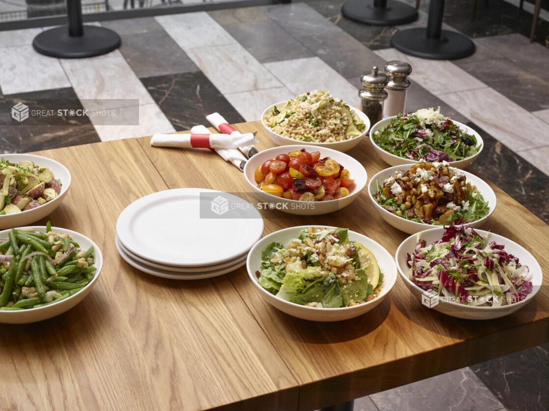 Assorted Italian Salads in Round White Ceramic Bowls on a Wooden Table in a Restaurant Setting