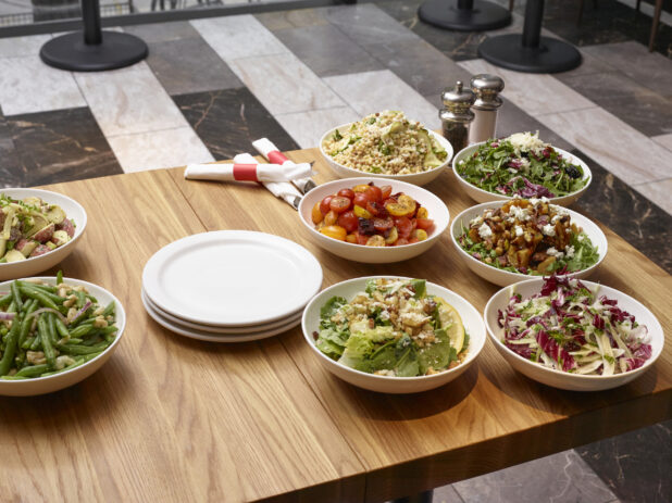 Assorted Italian Salads in Round White Ceramic Bowls on a Wooden Table in a Restaurant Setting