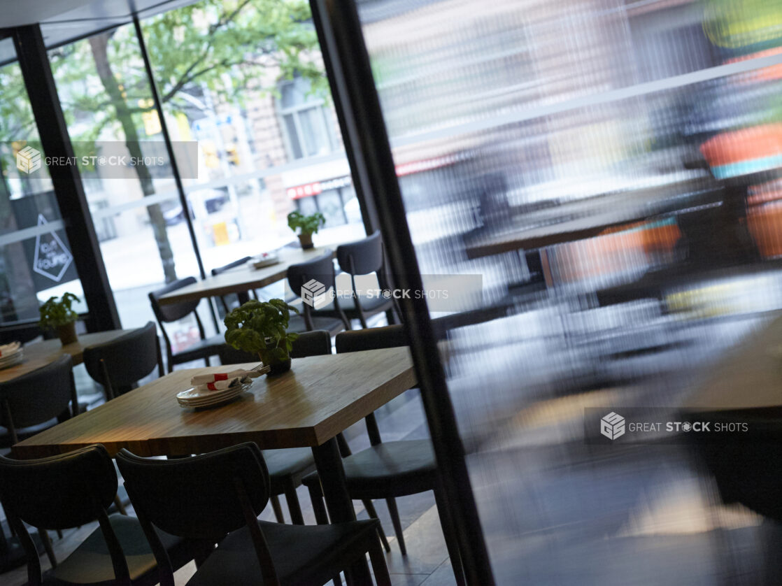 Interior of a Casual Restaurant with Wooden Tables and Potted Basil Plants, Overlooking a Busy City Street