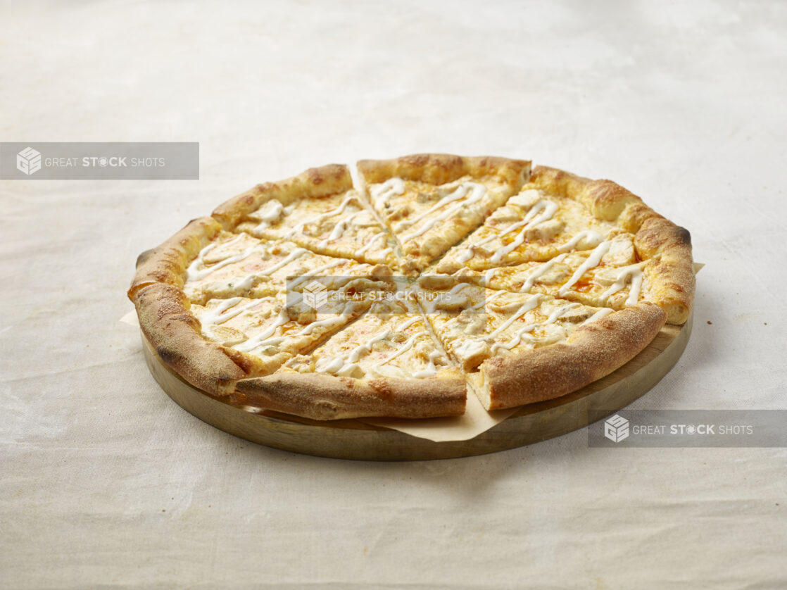 Sliced Buffalo chicken pizza with drizzled ranch on top on a wooden board with parchment paper