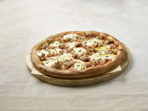 Whole meat and onion pizza with fresh basil on top on a wooden board with parchment paper