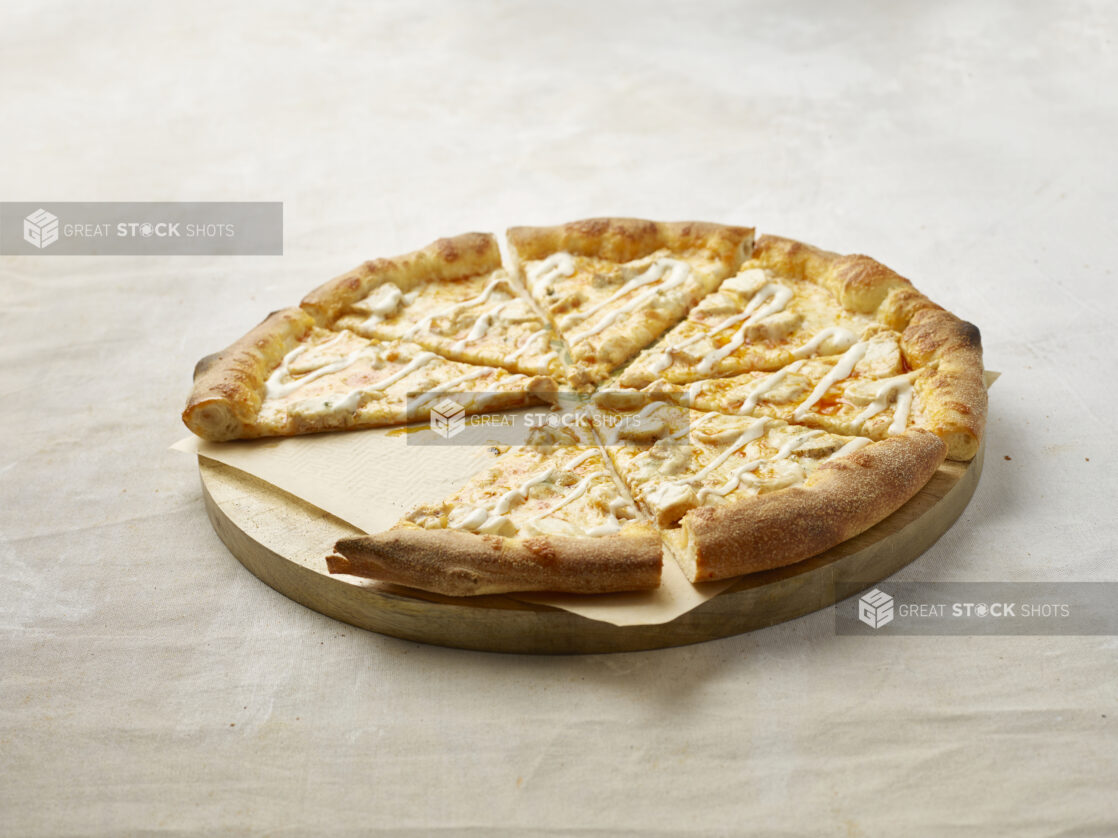 Sliced Buffalo chicken pizza with drizzled ranch on top with a slice missing on a wooden board with parchment paper