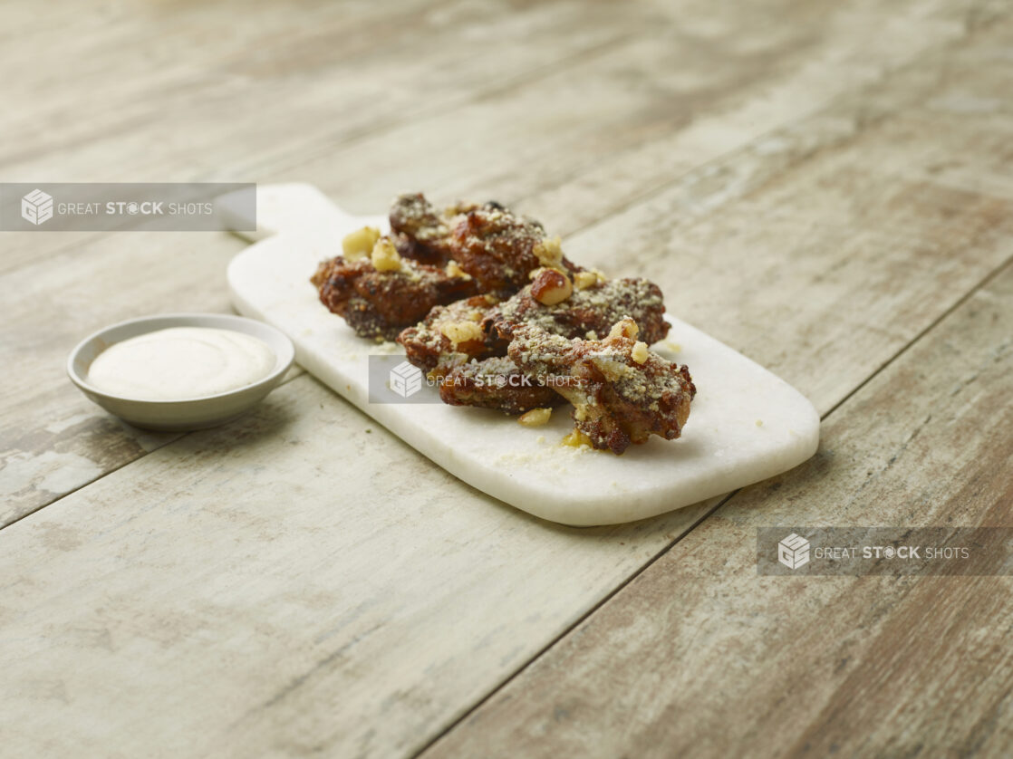 Dry rubbed garlic parmesan chicken wings on a marble board with a creamy dipping sauce on a wooden background