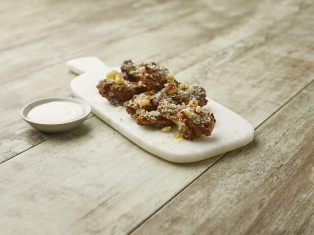 Dry rubbed garlic parmesan chicken wings on a marble board with a creamy dipping sauce on a wooden background