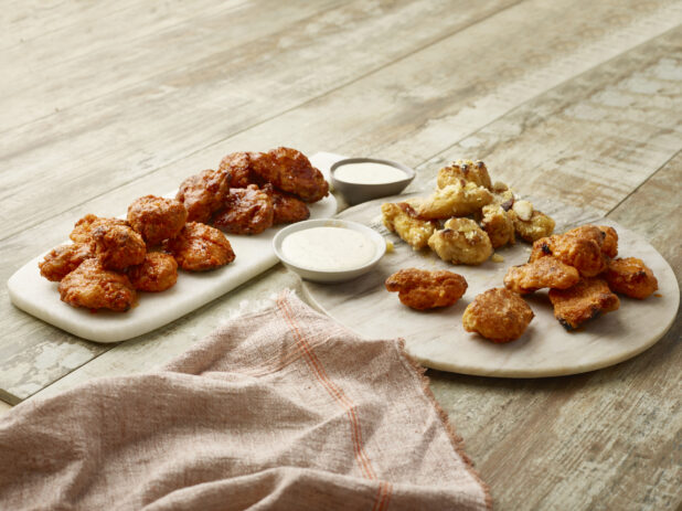 Four flavors of boneless wings with creamy dipping sauce on marble platters on a wooden background
