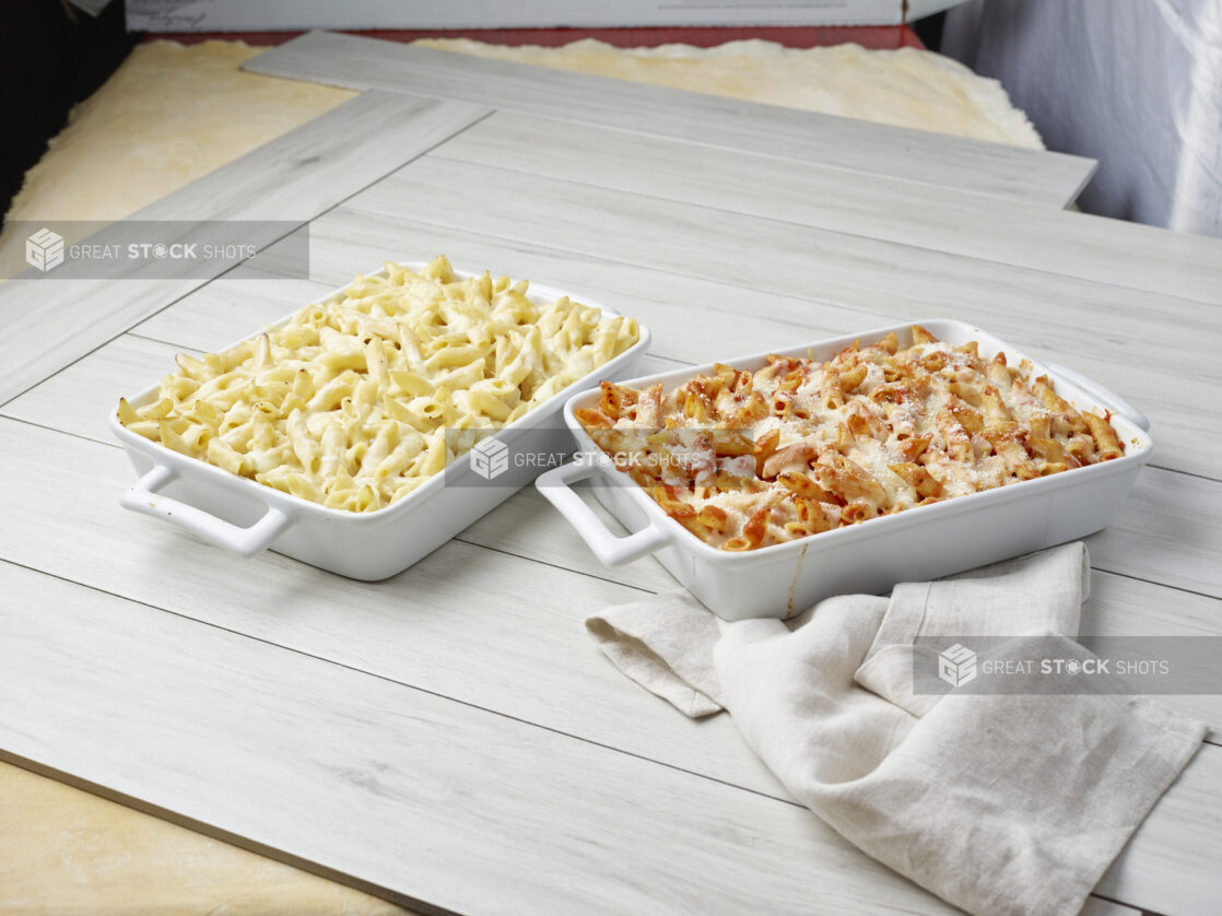 Two baked pasta dishes with melted cheese, one with white sauce and the other with tomato sauce on a light wooden background