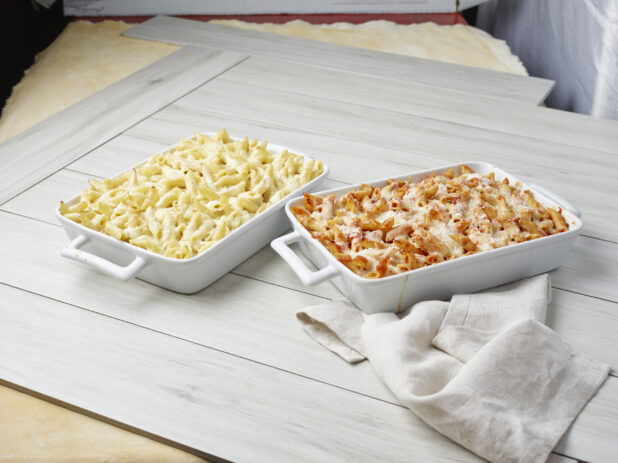 Two baked pasta dishes with melted cheese, one with white sauce and the other with tomato sauce on a light wooden background