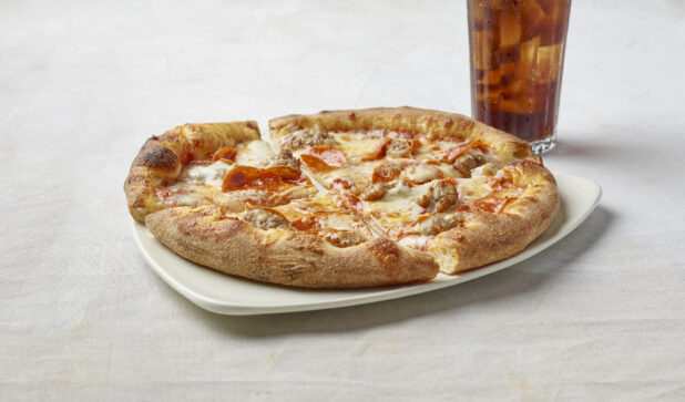 Small pizza with pepperoni and sausage on a plate with a glass of cola