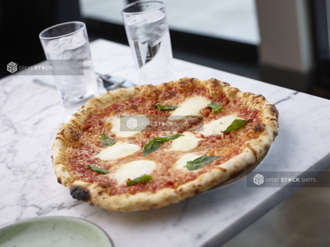 Sliced wood fire margherita pizza on a plate sitting on a white marble table in a restaurant