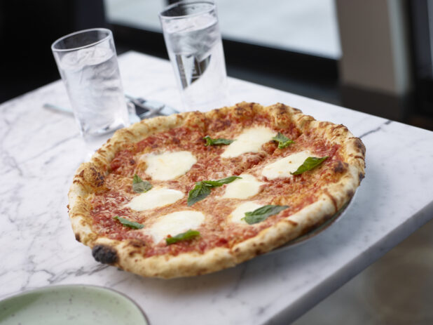 Sliced wood fire margherita pizza on a plate sitting on a white marble table in a restaurant