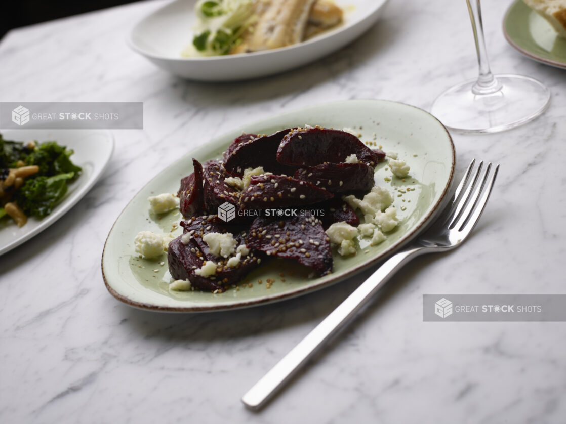 Sliced Roasted Beets with Feta Cheese Crumbles on a Green Ceramic Dish on a Marble Table