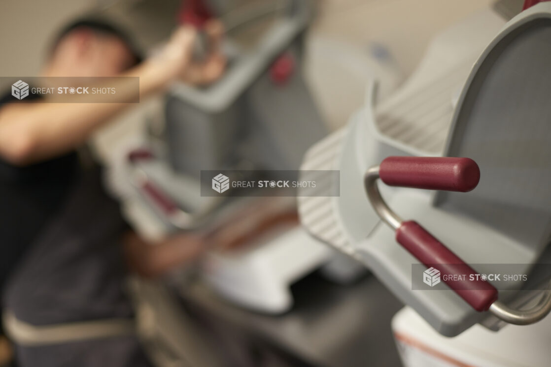 Close Up of a Commercial Grade Deli Meat Slicer with an Employee Slicing Meat in the Background in a Gourmet Grocery Store Setting