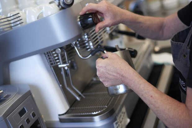 Close Up of a Barista's Hands Preparing a Latte on an Commercial Espresso Coffee Machine in a Cafe Located in a Gourmet Grocery Store