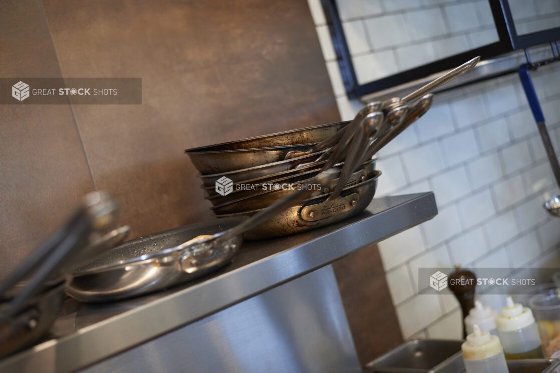 Sauté pans stacked on a shelf above a kitchen range, tilted angle