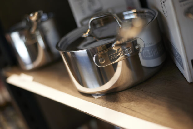 Stainless steel saucepan on a shelf, handle foreshortened and out of focus