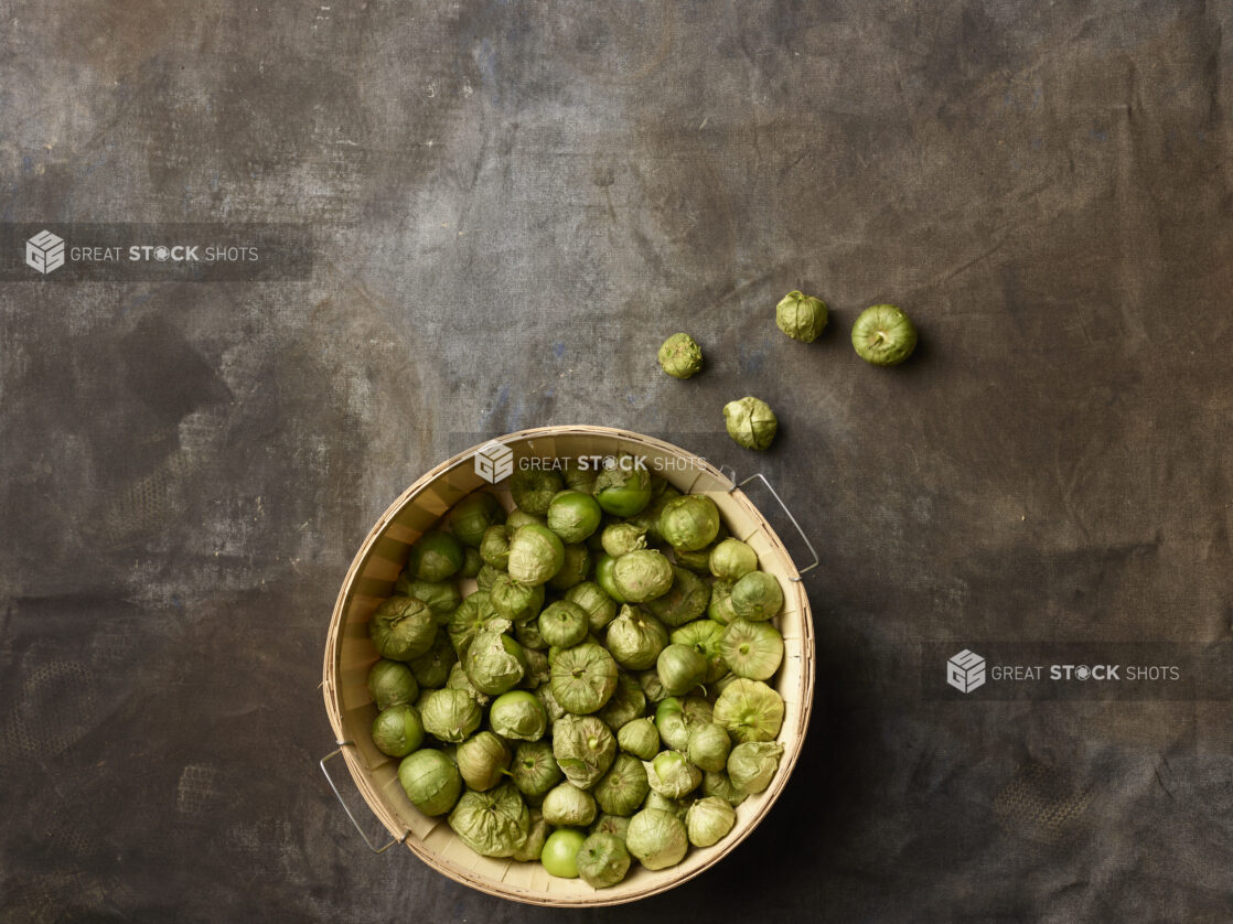 Bushel basket of tomatillos on a dark grey background