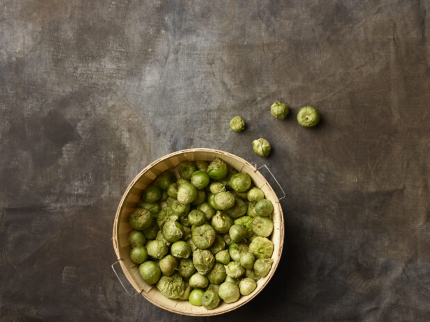 Bushel basket of tomatillos on a dark grey background