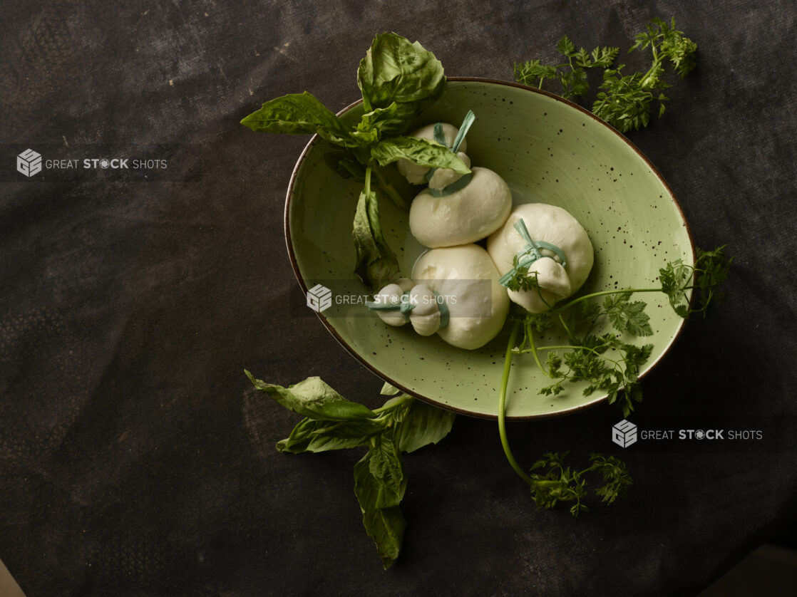 Three balls of Fresh Mozzarella Treccione in a green bowl surrounded by fresh herbs