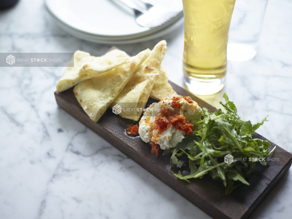 Appetizer Platter with House-Made Creamy Ricotta, Wood-Fired Flatbread and Baby Arugula on a Wooden Platter on a Marble Table