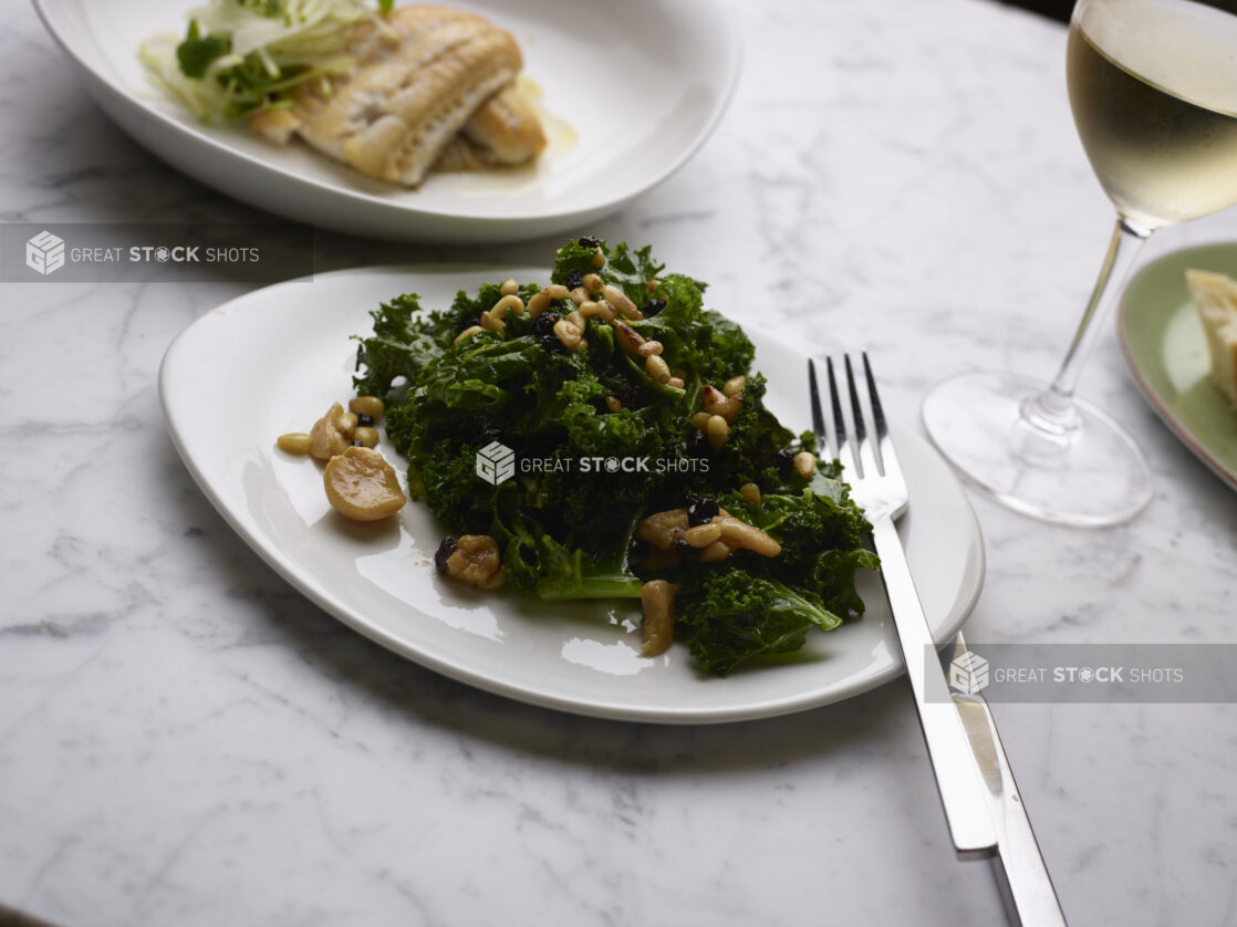 Sautéed Kale with Pine Nuts and Roasted Garlic on a White Ceramic Dish on a Marble Table