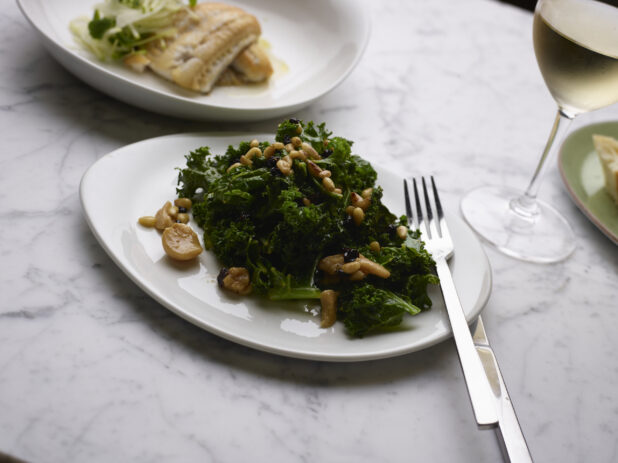 Sautéed Kale with Pine Nuts and Roasted Garlic on a White Ceramic Dish on a Marble Table