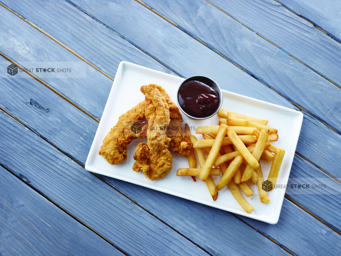 Overhead View of a Kid's Chicken Finger Combo Meal with Fries and a Side of BBQ Dipping Sauce on a White Rectangular Platter on a Painted Wood Surface