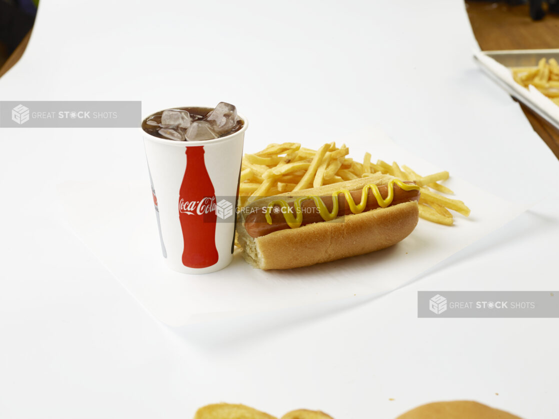 Hot Dog Combo with Yellow Mustard, French Fries and a Fountain Soda in a Paper Cup with Ice Cubes, on a White Background for Isolation