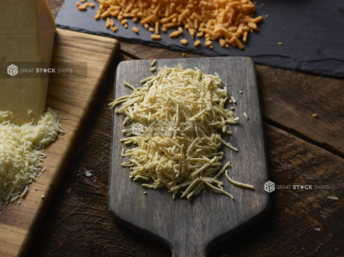 Shredded dairy-free cheese with various other grated cheeses on wood boards on a dark wood table