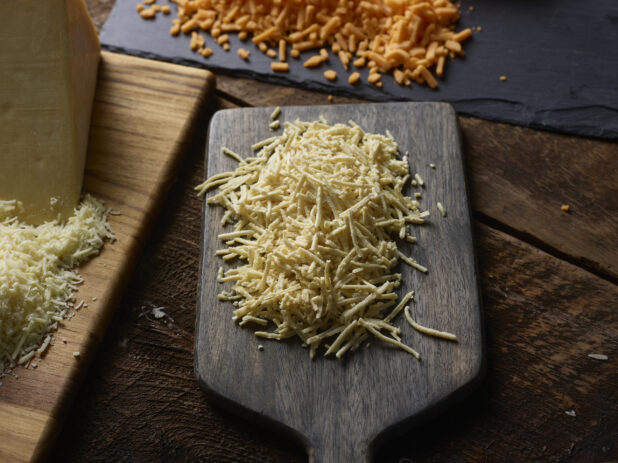 Shredded dairy-free cheese with various other grated cheeses on wood boards on a dark wood table