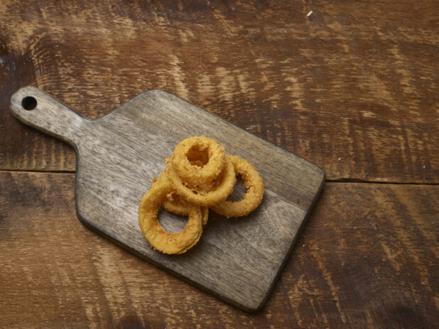 Fried onion rings on a wooden board on a rustic wooden background