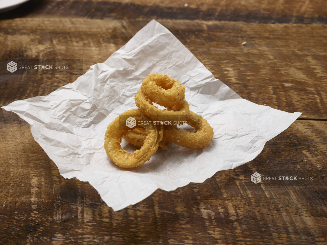 Fried onion rings on parchment paper on a rustic wooden background