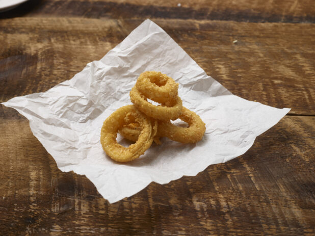 Fried onion rings on parchment paper on a rustic wooden background