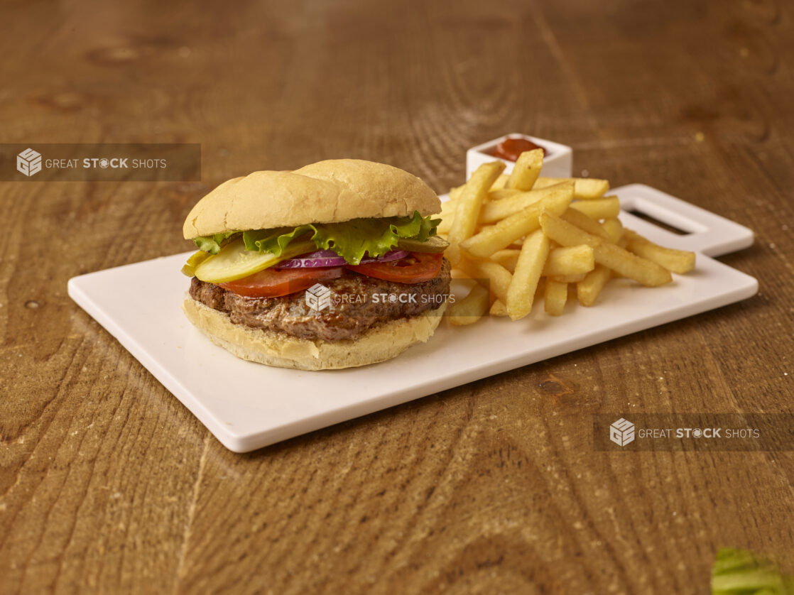 Close Up of a White Ceramic Platter with a Hamburger and French Fries Kids Meal Combo and a Side of Ketchup on a Brown Wooden Table Surface