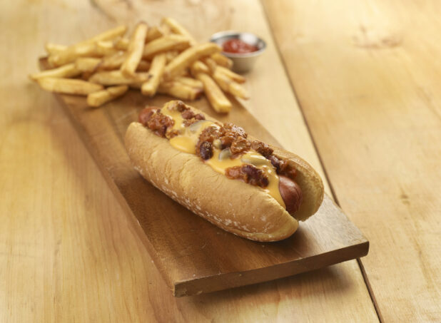 Chili dog with french fries on a wooden board on a wooden table with a small ramekin of ketchup