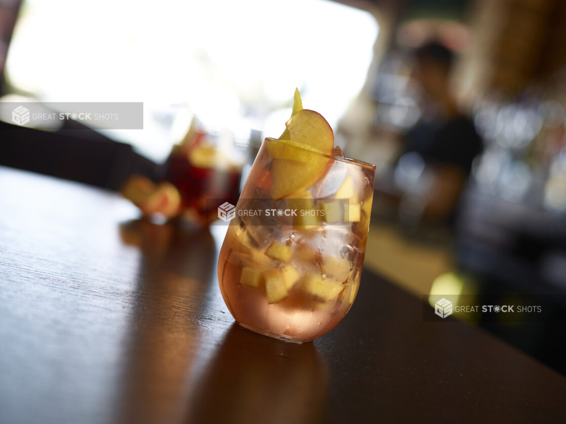 Vodka Peach Summer Cocktail on the Rocks in a Glass Tumbler on a Dark Wooden Table Top in a Restaurant Interior Setting