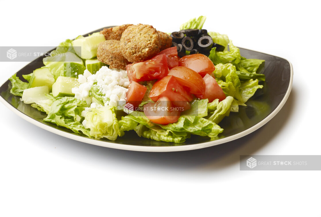 Plain Greek Salad with Chopped Tomatoes, Cucumber, Black Olives, Feta and Falafel Balls on a Square Black Ceramic Dish, on a White Background for Isolation