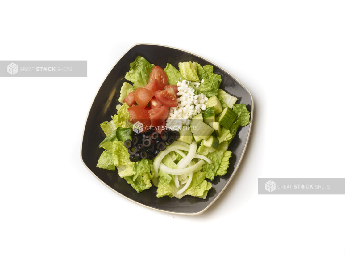 Overhead View of a Plain Greek Salad with Chopped Tomatoes, Cucumber, Black Olives, Feta and White Onions on a Square Black Ceramic Dish, on a White Background for Isolation