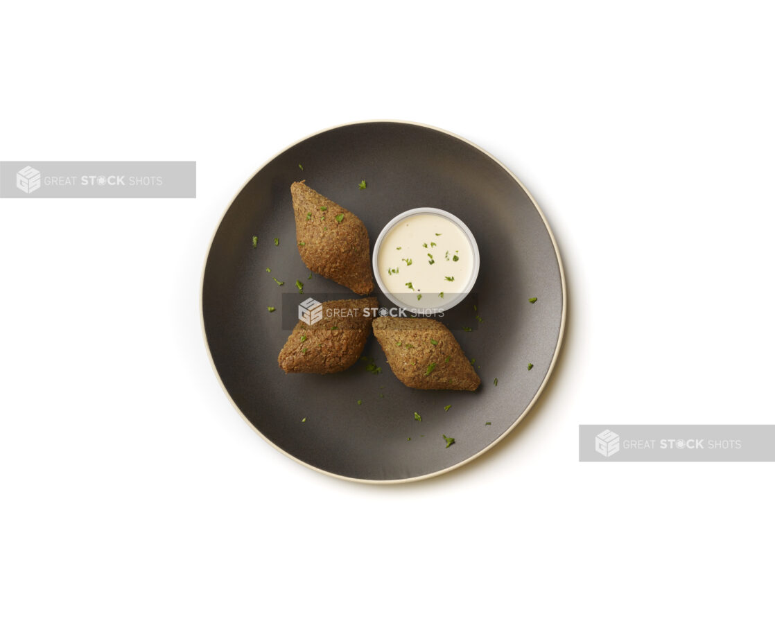 Overhead View of Diamond Shaped Falafel Balls on a Black Ceramic Dish with a Side of Creamy Tahini Dipping Sauce, Shot on a White Background for Isolation