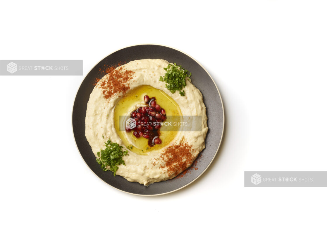 Overhead View of a Plate of Baba Ganoush Creamy Eggplant Dip with EVOO, Pomegranate Seeds, Fresh Chopped Parsley and Paprika Powder, Shot on White for Isolation