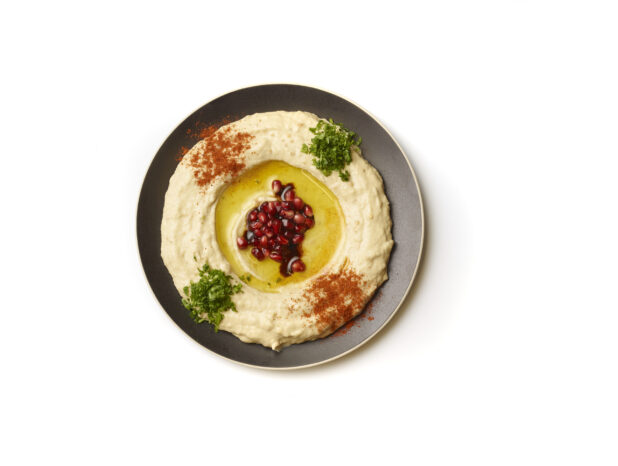 Overhead View of a Plate of Baba Ganoush Creamy Eggplant Dip with EVOO, Pomegranate Seeds, Fresh Chopped Parsley and Paprika Powder, Shot on White for Isolation