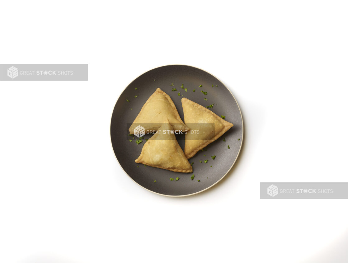 Overhead View of Vegetarian Samosas on a Round Black Ceramic Dish with Chopped Parsley Garnish, on a White Background for Isolation