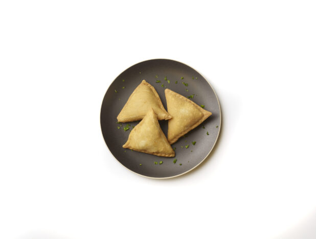 Overhead View of Vegetarian Samosas on a Round Black Ceramic Dish with Chopped Parsley Garnish, on a White Background for Isolation