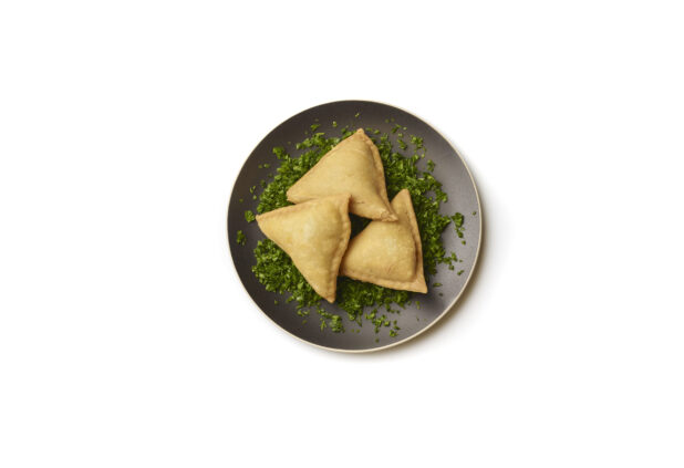 Overhead View of Vegetarian Samosas on a Bed of Chopped Fresh Parsley and Round Black Ceramic Dish, on a White Background for Isolation