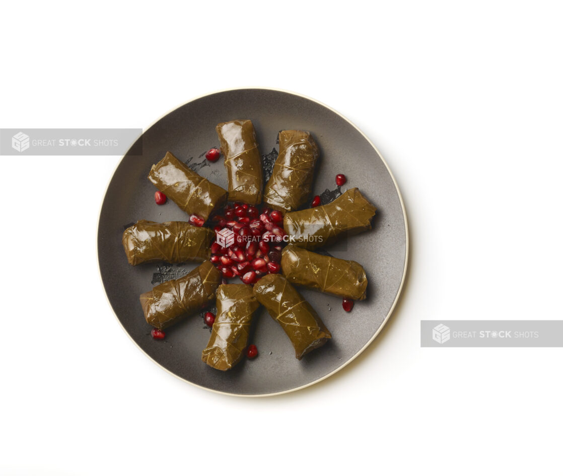 Overhead View of a Round Black Ceramic Dish of Stuffed Grapevine Leaves and Pomegranate Seeds, on a White Background for Isolation