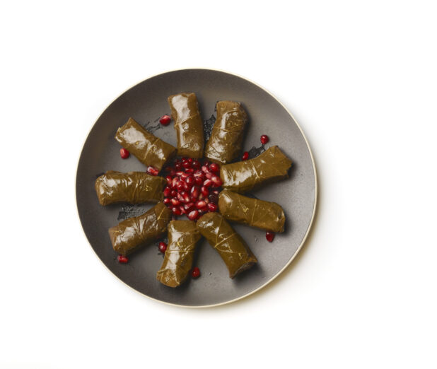 Overhead View of a Round Black Ceramic Dish of Stuffed Grapevine Leaves and Pomegranate Seeds, on a White Background for Isolation