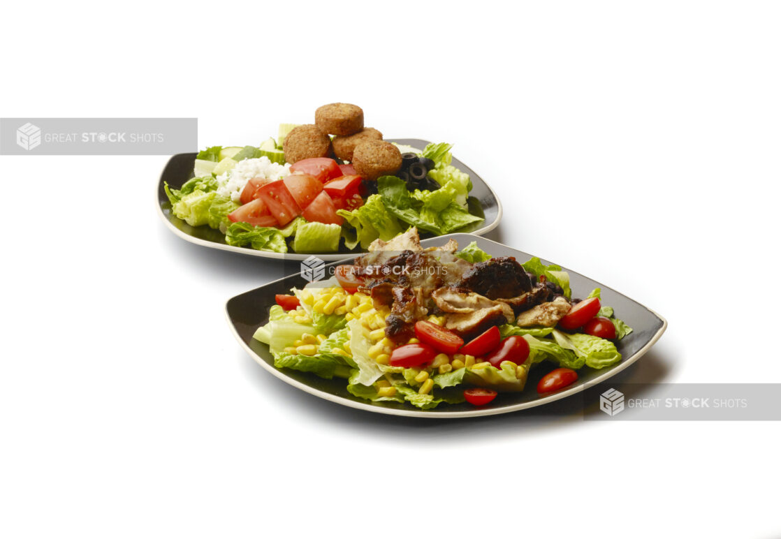 Chicken Shawarma Salad with Corn and Black Beans and a Greek Salad with Falafel Balls and Feta Cheese on Square Black Ceramic Dishes, on a White Background for Isolation