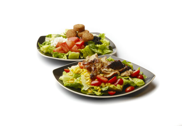 Chicken Shawarma Salad with Corn and Black Beans and a Greek Salad with Falafel Balls and Feta Cheese on Square Black Ceramic Dishes, on a White Background for Isolation